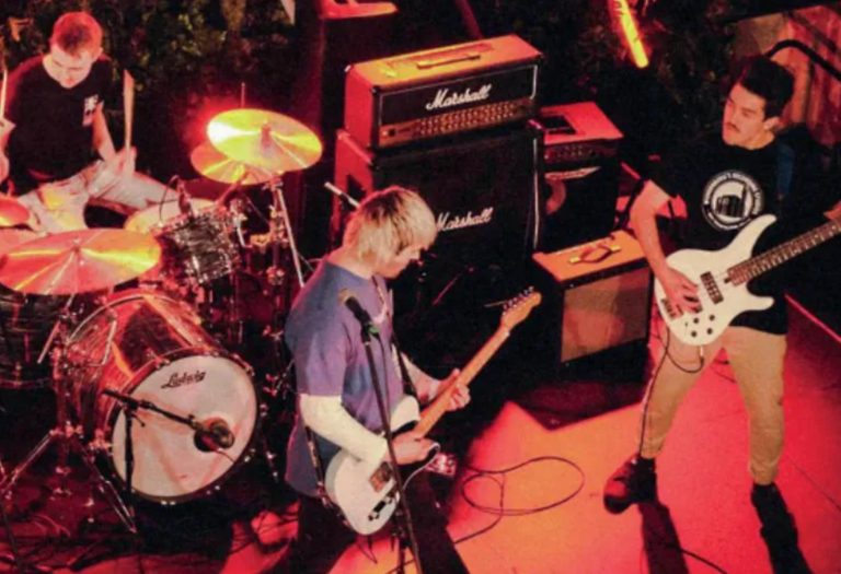 Live band performing on stage under red lighting at Space Jams Festival in South Australia with drummer, guitarist, and bass player.